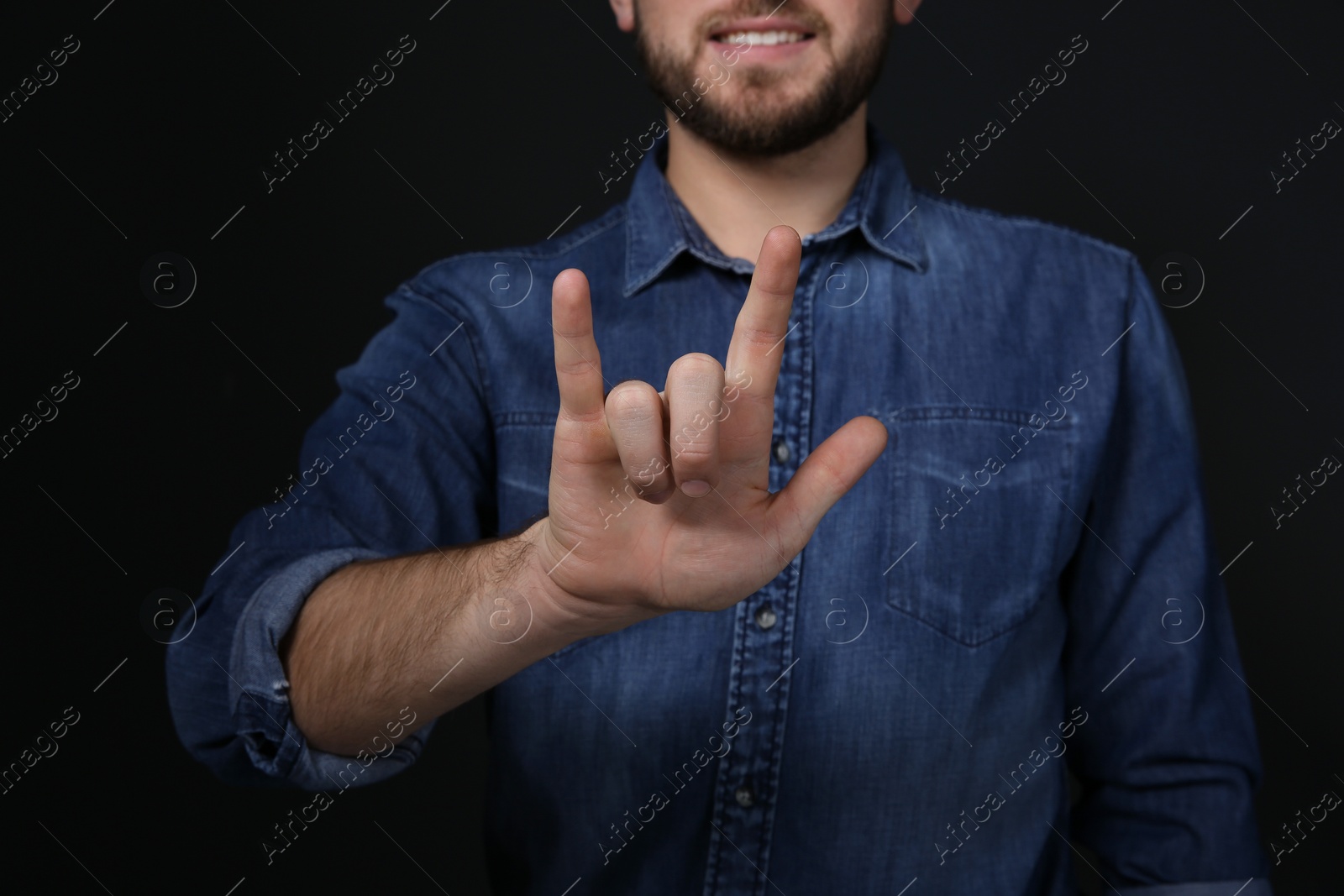 Photo of Man showing I LOVE YOU gesture in sign language on black background, closeup