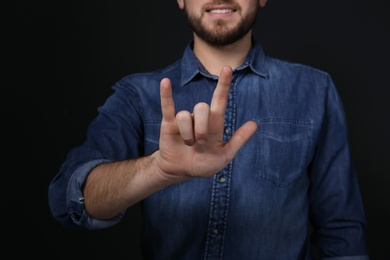 Photo of Man showing I LOVE YOU gesture in sign language on black background, closeup