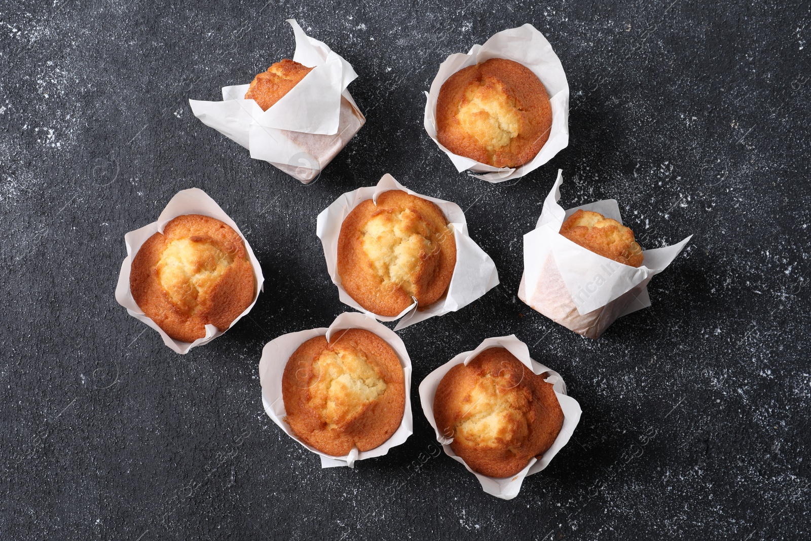 Photo of Delicious sweet muffins on black textured table, flat lay