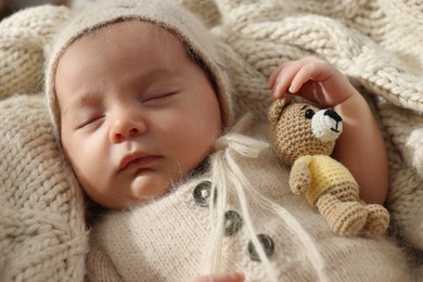 Adorable newborn baby with toy bear sleeping on knitted plaid, closeup