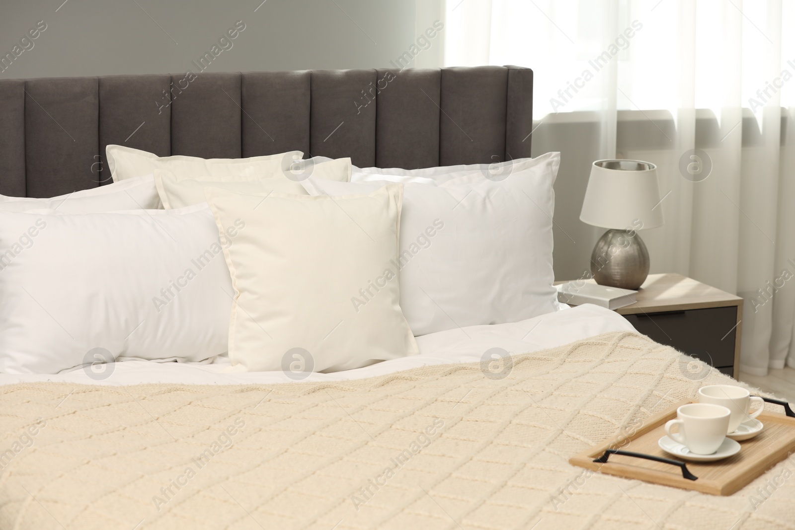 Photo of Many soft white pillows and knitted blanket on bed indoors