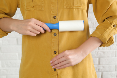 Photo of Woman cleaning yellow shirt with lint roller against white brick wall, closeup