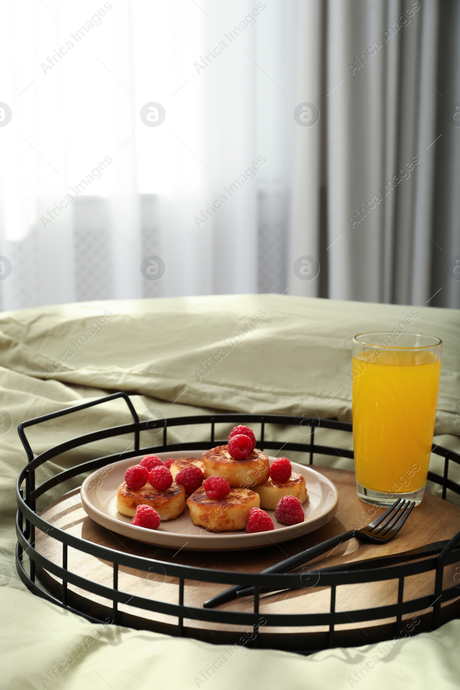 Photo of Tasty breakfast served in bedroom. Cottage cheese pancakes with fresh raspberries and juice on tray