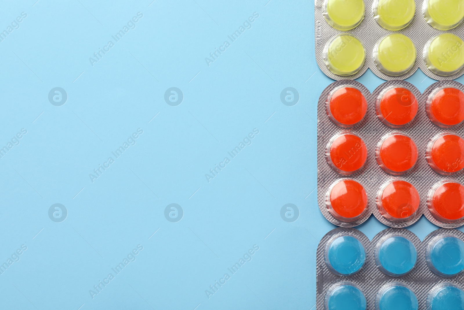 Photo of Blisters with colorful cough drops on light blue background, flat lay. Space for text