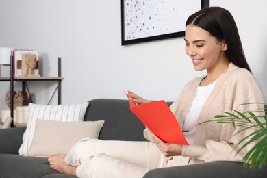 Photo of Happy woman reading greeting card on sofa in living room