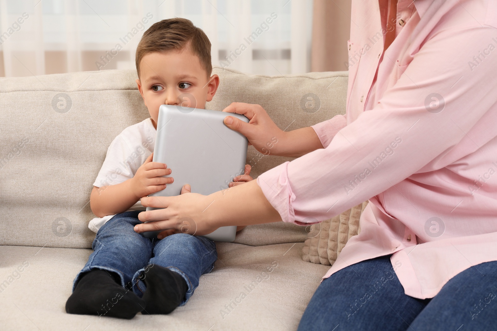 Photo of Internet addiction. Mother taking away tablet from her little son on sofa at home, closeup