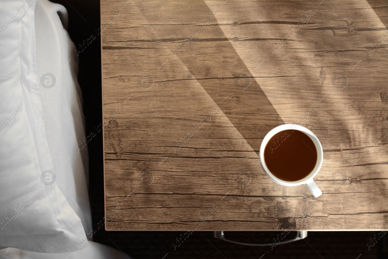 Photo of Cup of coffee on wooden night stand near bed in morning, top view. Space for text
