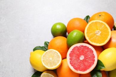 Photo of Pile of different fresh citrus fruits and leaves on grey textured table, flat lay. Space for text