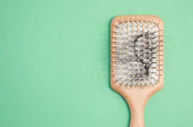 Photo of Wooden brush with lost hair on green background, top view. Space for text