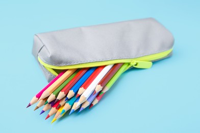 Many colorful pencils in pencil case on light blue background, closeup