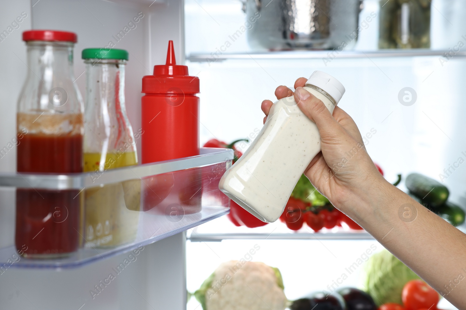 Photo of Young woman taking bottle of sauce out of refrigerator, closeup