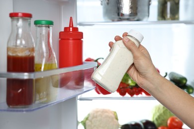 Young woman taking bottle of sauce out of refrigerator, closeup