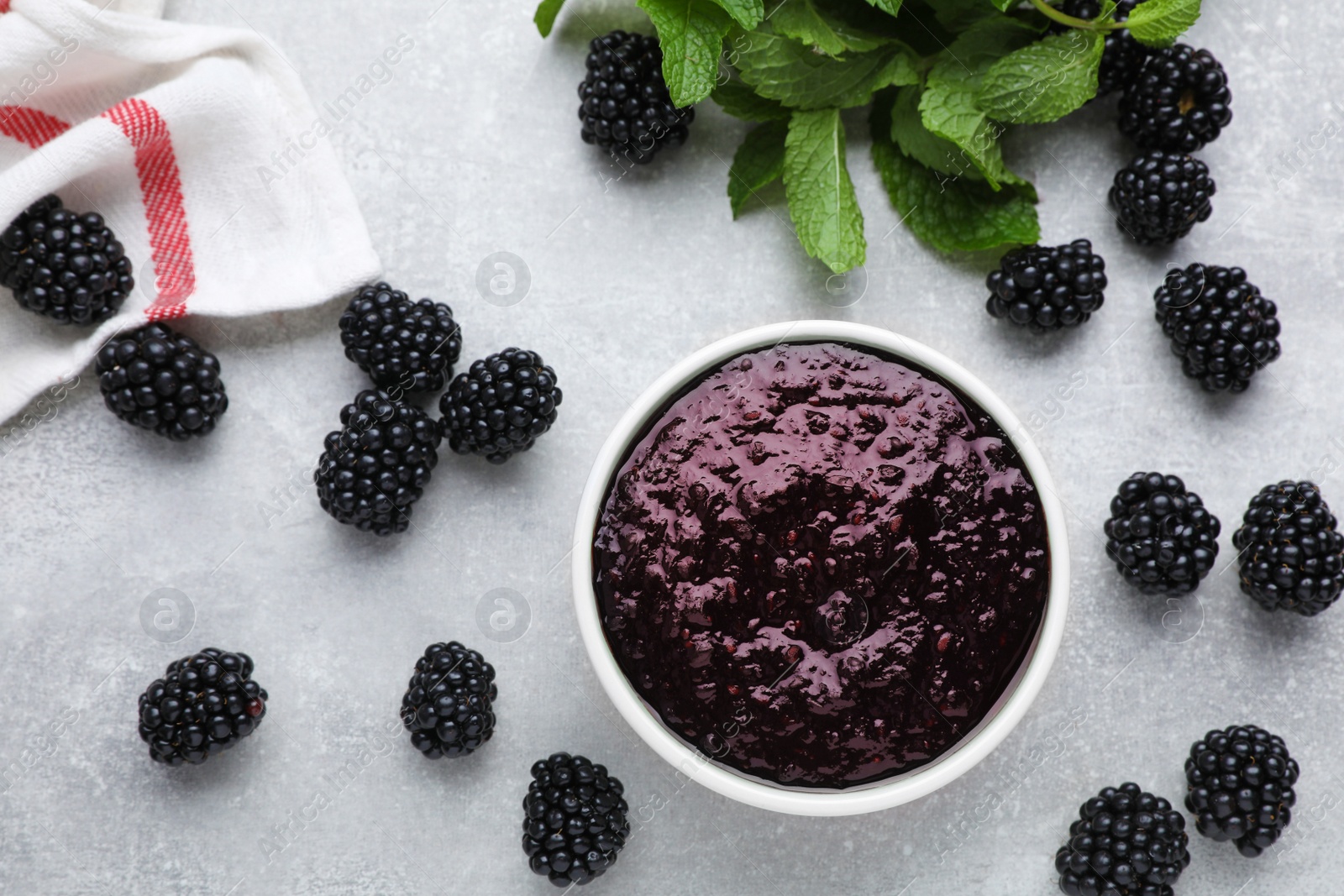 Photo of Blackberry puree in bowl and fresh berries on light grey table, flat lay