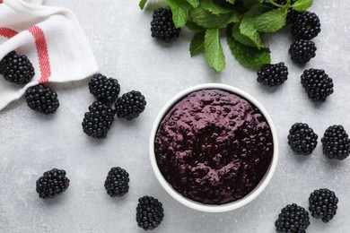 Blackberry puree in bowl and fresh berries on light grey table, flat lay