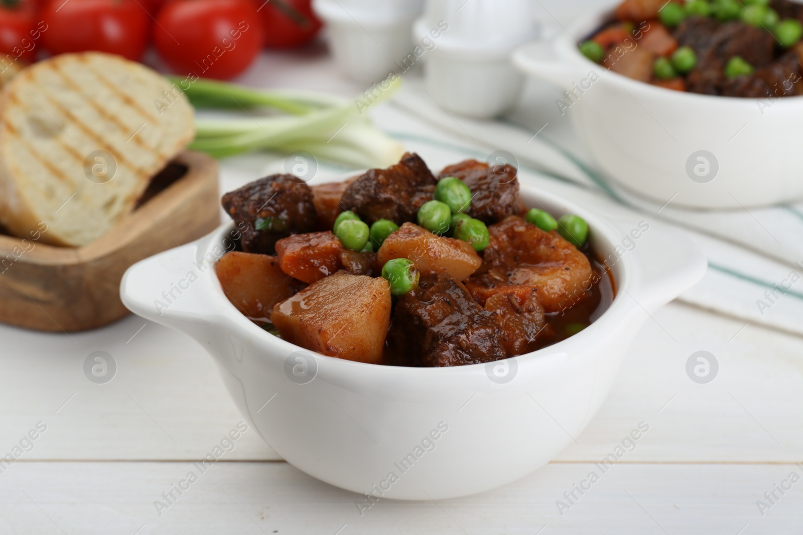 Photo of Delicious beef stew with carrots, peas and potatoes on white wooden table, closeup