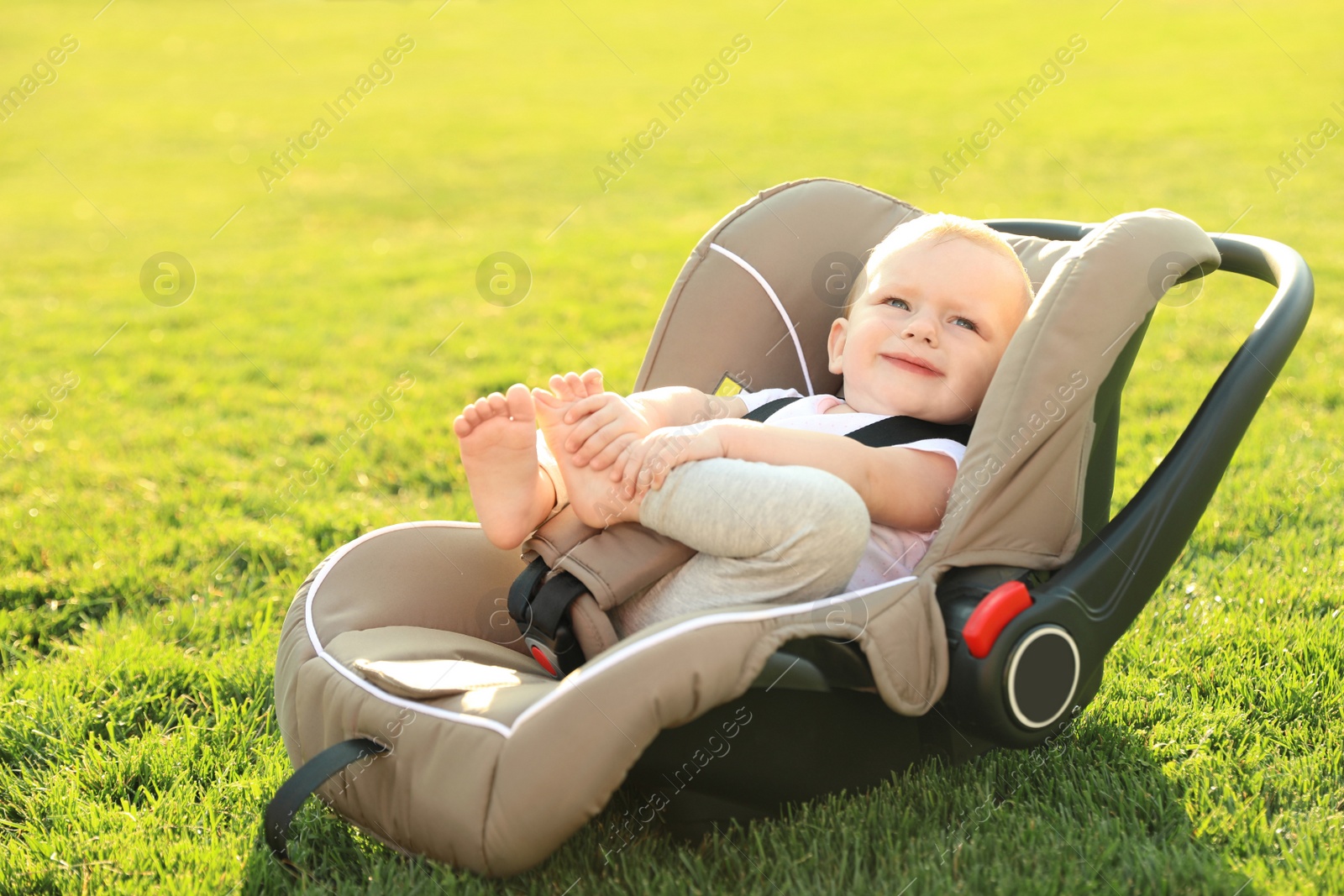 Photo of Adorable baby in child safety seat on green grass