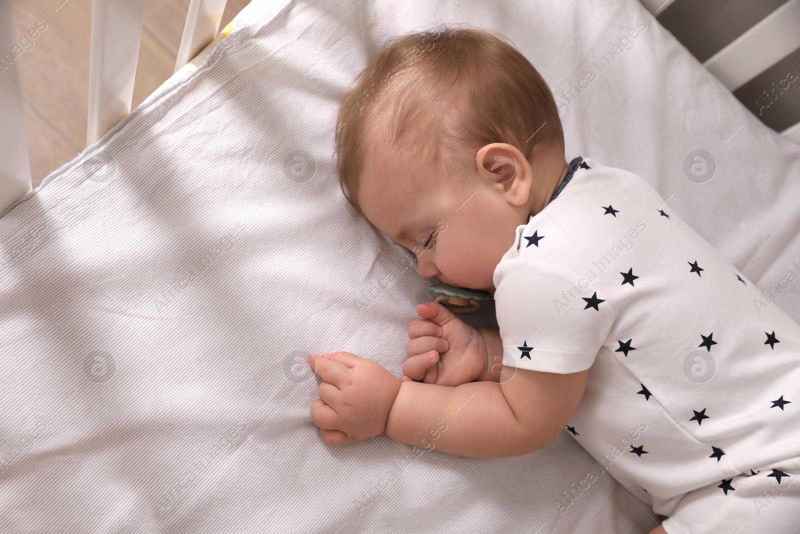 Photo of Adorable little baby with pacifier sleeping in crib, above view