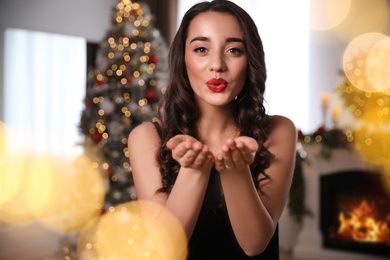 Photo of Beautiful young woman wearing elegant dress blowing kiss in room decorated for Christmas