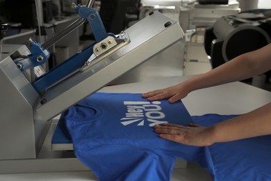 Photo of Printing logo. Woman with t-shirt using heat press at white table, closeup
