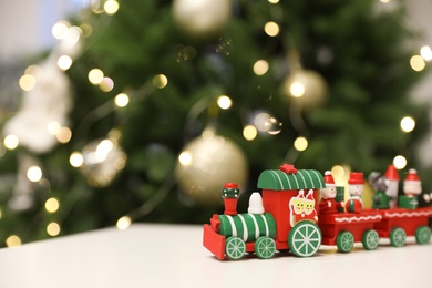 Bright toy train on white table near Christmas tree, space for text