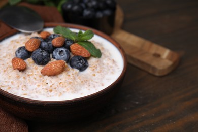 Tasty wheat porridge with milk, blueberries and almonds in bowl on wooden table, closeup