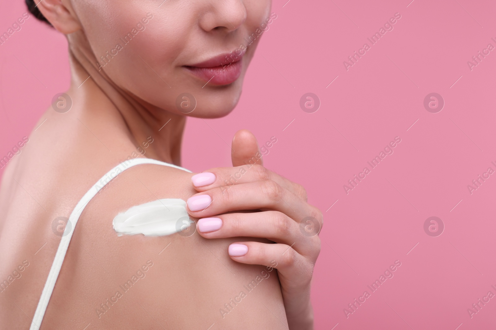 Photo of Woman with smear of body cream on her shoulder against pink background, closeup. Space for text