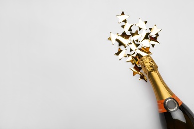 Flat lay composition with confetti and bottle of champagne on light background. Space for text