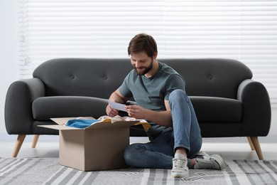 Photo of Happy man with greeting card near parcel at home. Internet shopping