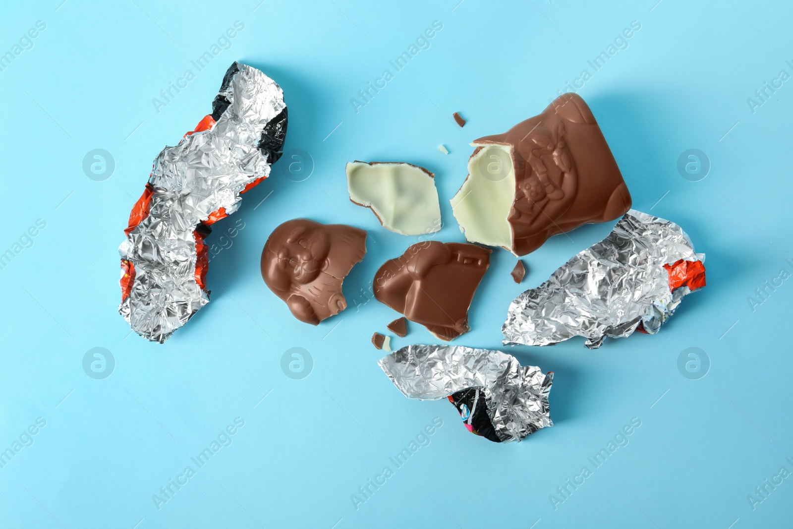 Photo of Broken chocolate Santa Claus and foil wrapper on light blue background, flat lay