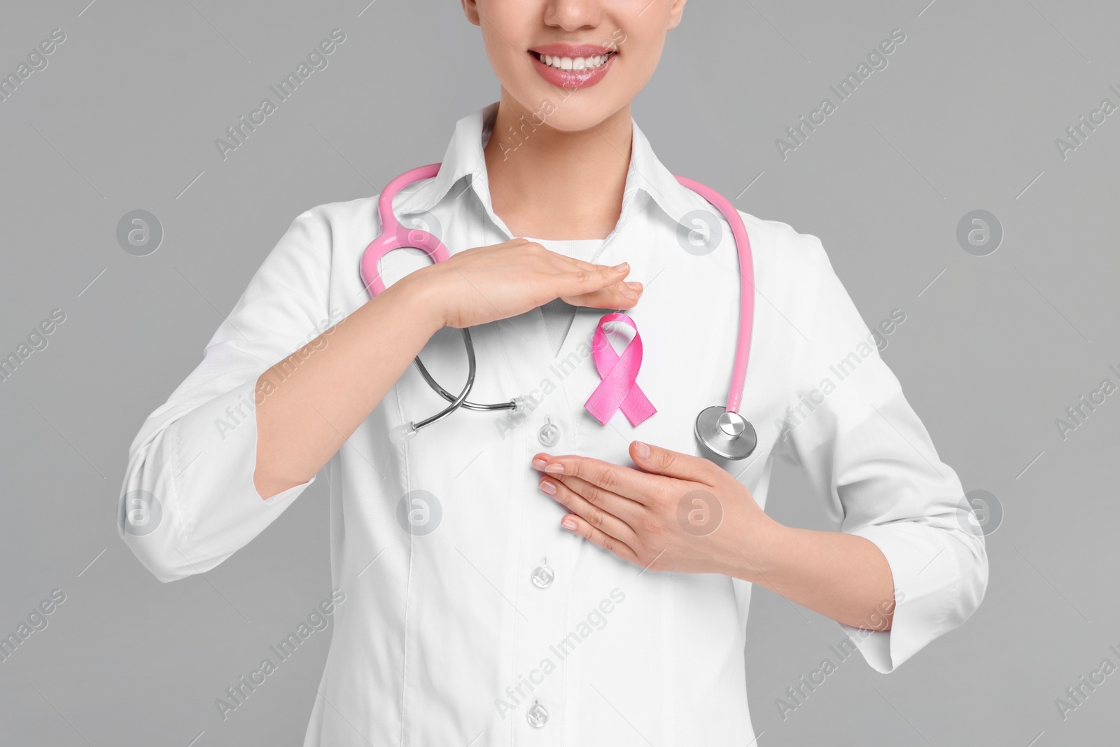 Photo of Mammologist with pink ribbon on gray background, closeup. Breast cancer awareness