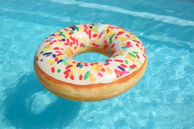 Photo of Bright inflatable doughnut ring floating in swimming pool on sunny day