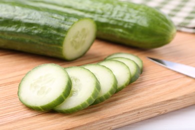 Fresh cucumbers and knife on wooden cutting board, closeup