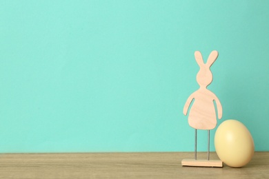 Cute wooden Easter bunny and dyed egg on table against color background, space for text