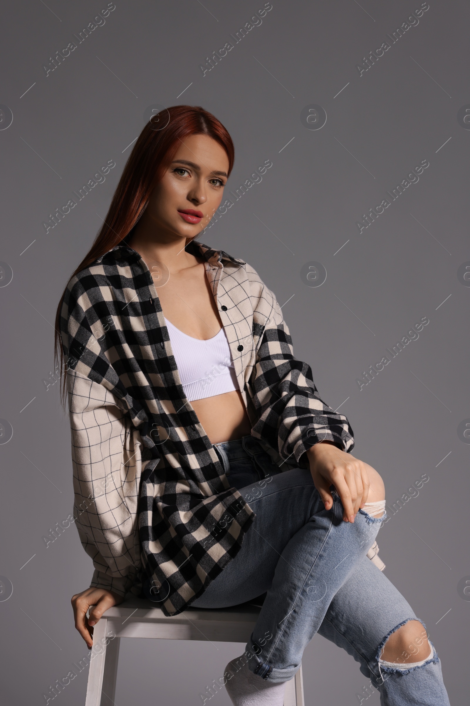 Photo of Beautiful young woman sitting on white stool against gray background
