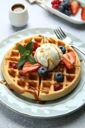 Photo of Delicious Belgian waffles with ice cream, berries and caramel sauce served on grey table, closeup