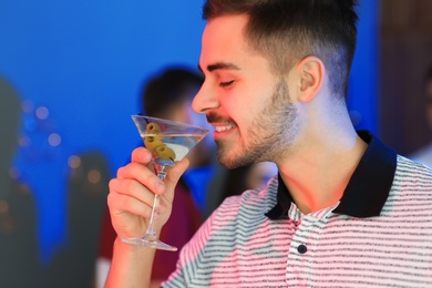 Young man with glass of martini cocktail at party, space for text