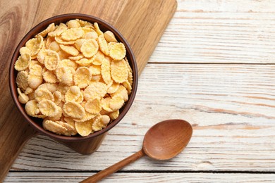 Photo of Bowl of tasty corn flakes and spoon on wooden table, top view. Space for text