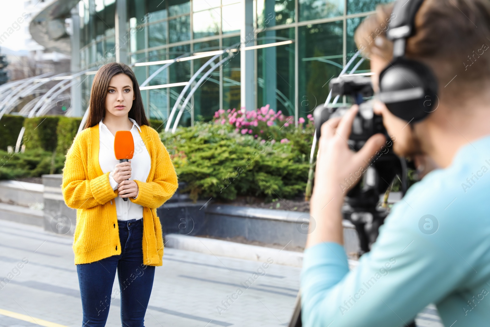 Photo of Young journalist and video operator working on city street