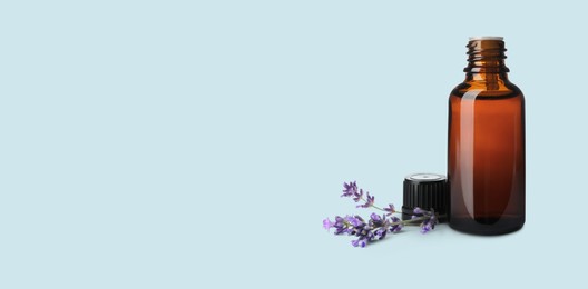 Image of Bottle of lavender essential oil and flowers on pale light blue background, space for text. Banner design