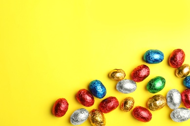 Chocolate eggs wrapped in colorful foil on yellow background, flat lay. Space for text