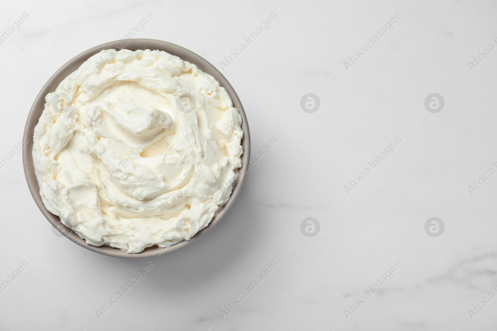 Photo of Bowl of tasty cream cheese on white table, top view. Space for text