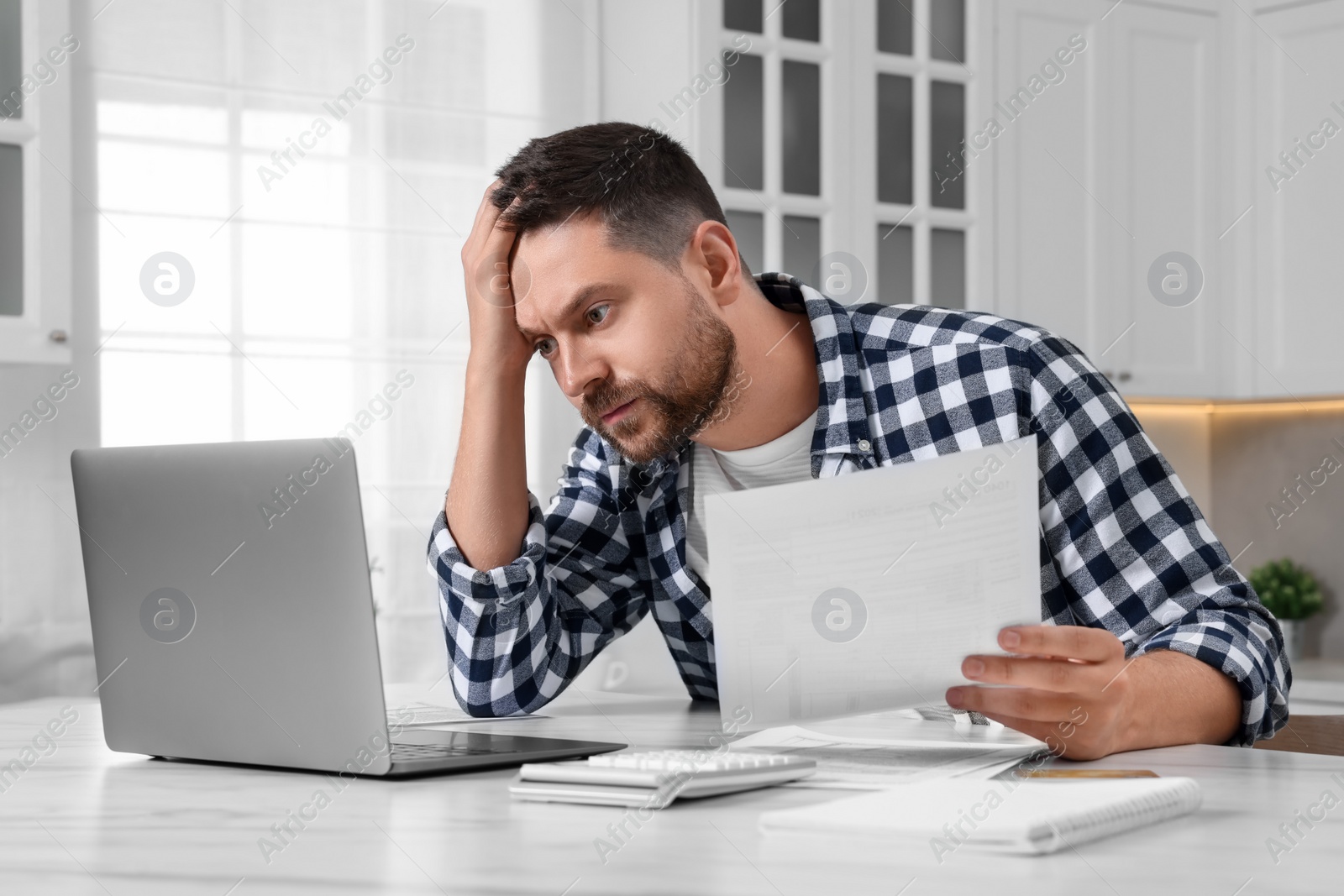 Photo of Man with laptop doing taxes at table in kitchen