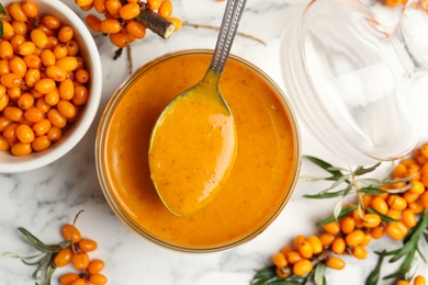 Photo of Delicious sea buckthorn jam and fresh berries on white marble table, flat lay