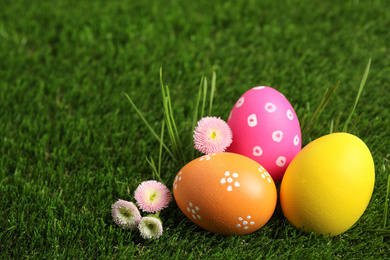 Colorful Easter eggs and daisy flowers on green grass. Space for text