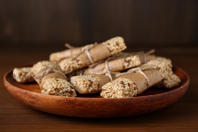 Photo of Plate with tasty sesame seed bars on wooden table, closeup