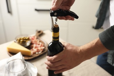 Photo of Man opening wine bottle with corkscrew at table indoors, closeup