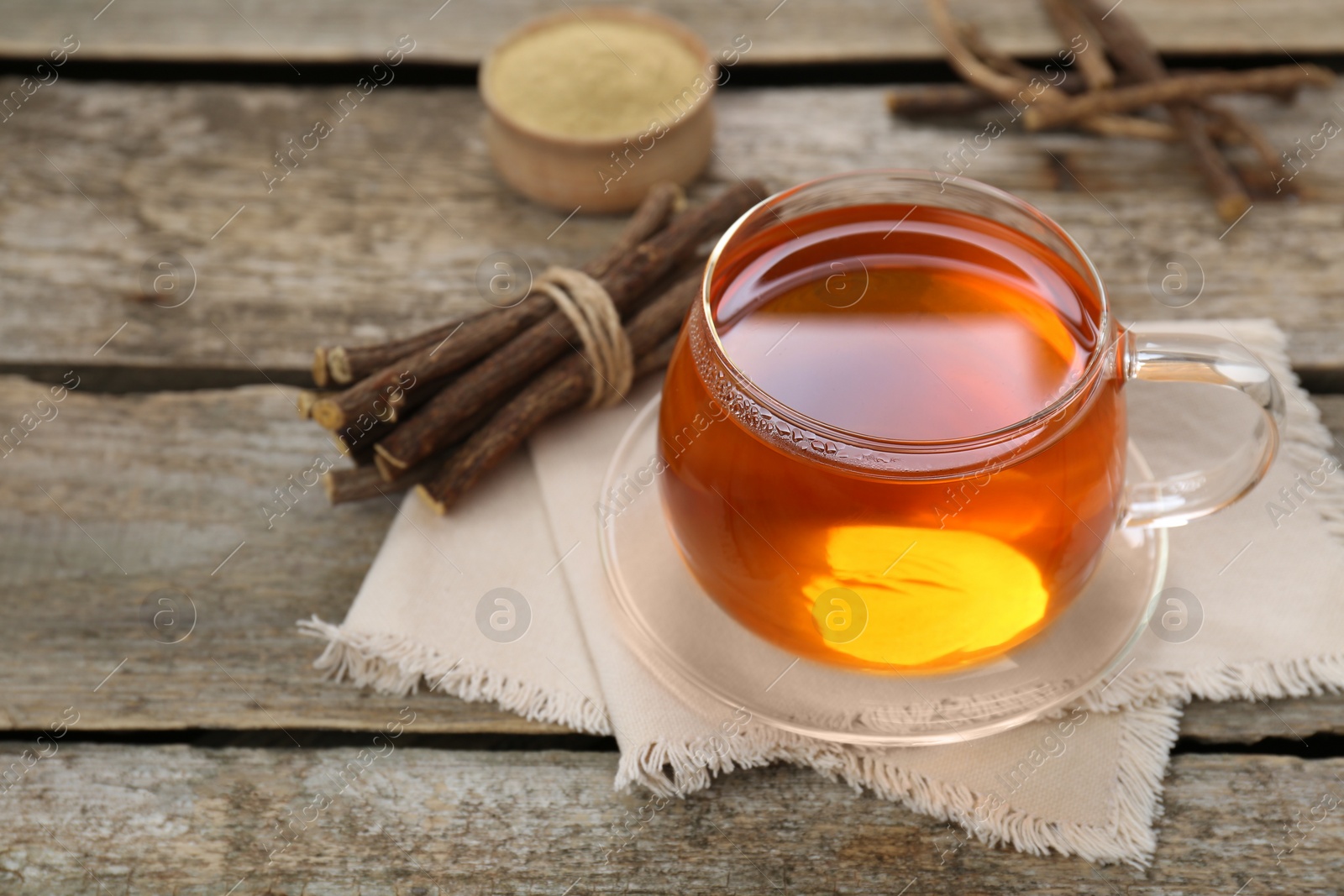 Photo of Aromatic licorice tea in cup and dried sticks of licorice root on wooden table. Space for text