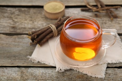 Aromatic licorice tea in cup and dried sticks of licorice root on wooden table. Space for text