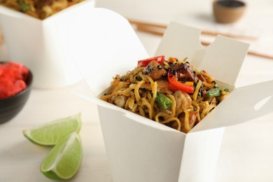 Photo of Box of wok noodles with vegetables and meat on white table, closeup