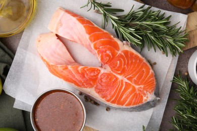 Photo of Fresh fish, rosemary and marinade on brown textured table, flat lay